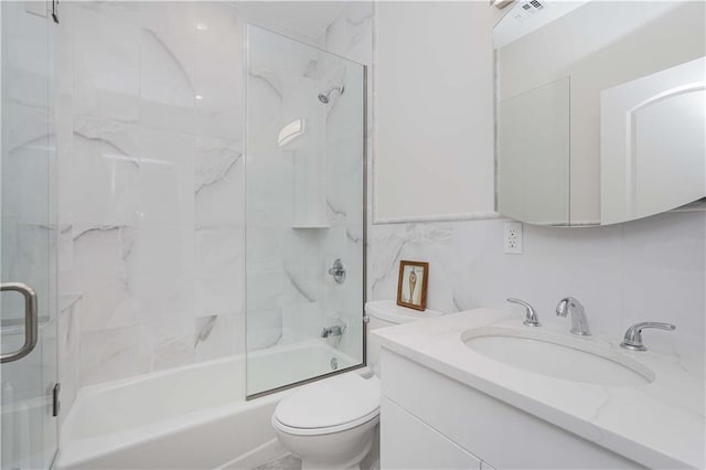 full bathroom with visible vents, bath / shower combo with glass door, toilet, vanity, and tile walls