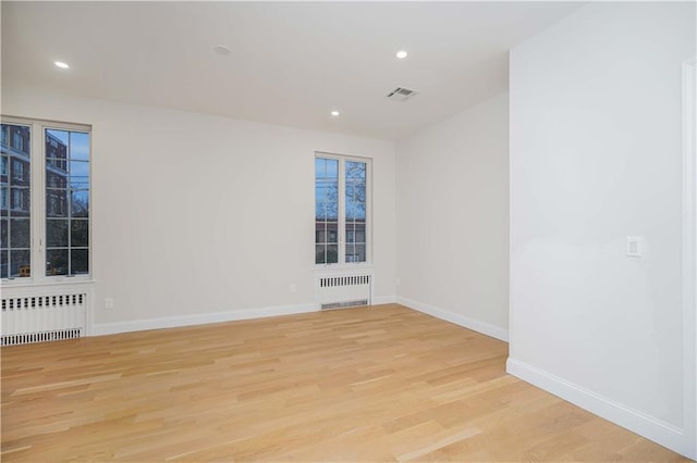 empty room featuring radiator, light wood finished floors, baseboards, and visible vents