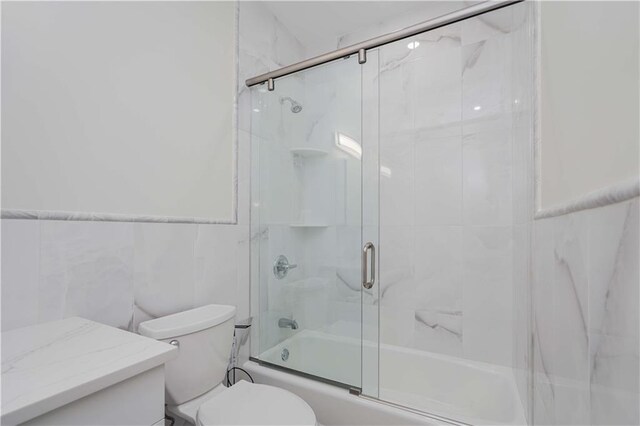 full bathroom featuring enclosed tub / shower combo, vanity, toilet, and tile walls