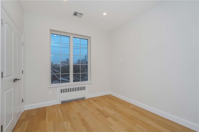 spare room featuring recessed lighting, radiator, visible vents, wood finished floors, and baseboards