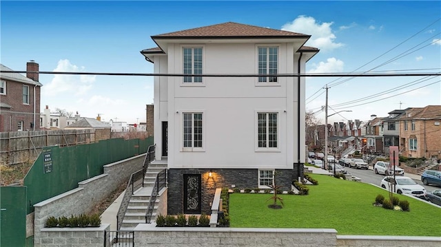 view of front facade featuring a residential view, fence, a front lawn, and stucco siding