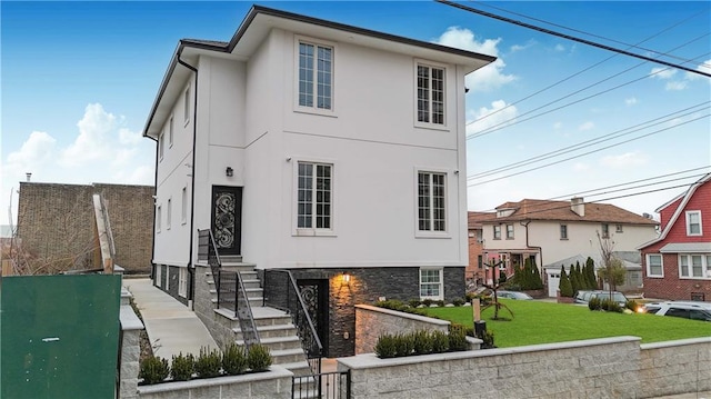 view of front of house with stone siding, a front lawn, and stucco siding