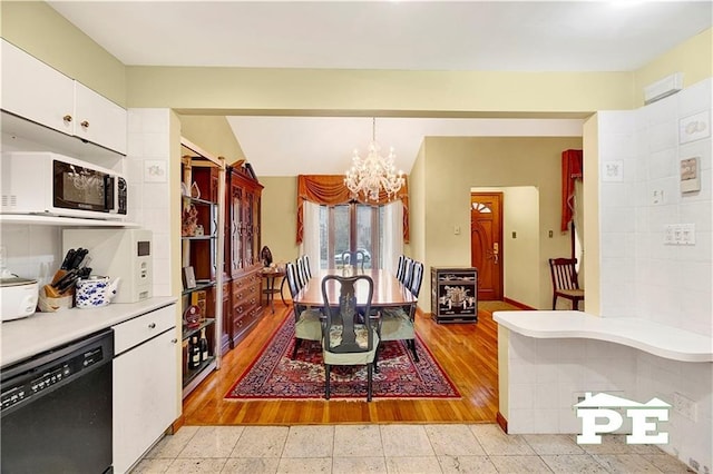 kitchen with black dishwasher, a notable chandelier, light countertops, white microwave, and white cabinetry