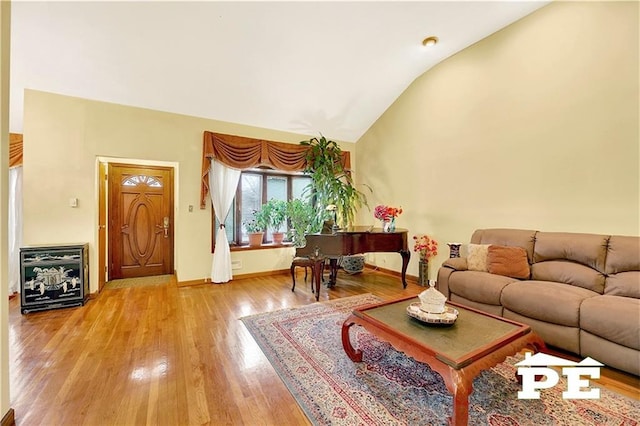 living area with high vaulted ceiling, light wood finished floors, and baseboards