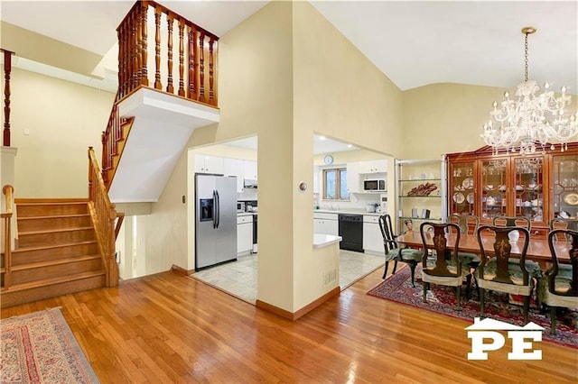 dining space featuring light wood-style floors, stairs, high vaulted ceiling, and an inviting chandelier