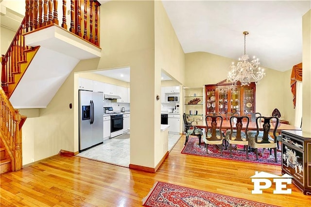 dining area with light wood-type flooring, high vaulted ceiling, stairway, and a chandelier