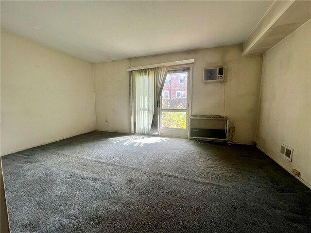 spare room featuring dark colored carpet, an AC wall unit, and heating unit