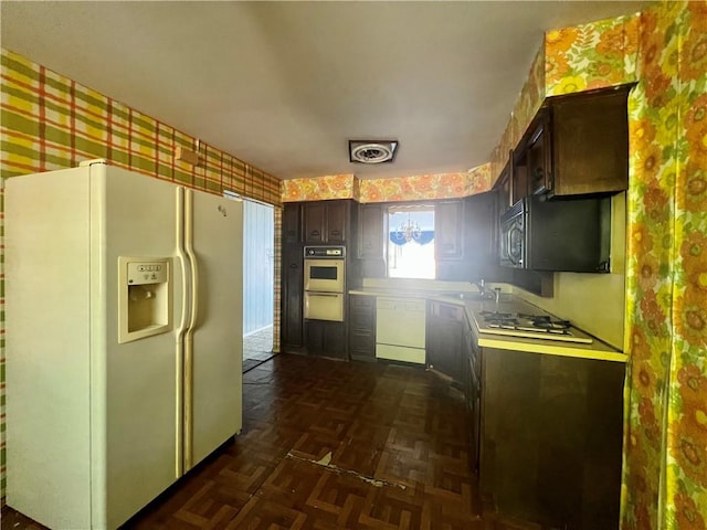 kitchen featuring wallpapered walls, dark brown cabinetry, white appliances, a warming drawer, and a sink