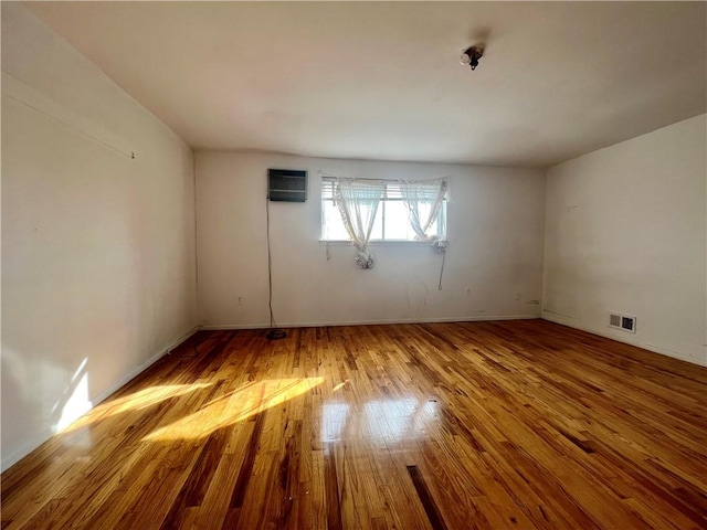 unfurnished room with hardwood / wood-style floors, a wall unit AC, and visible vents