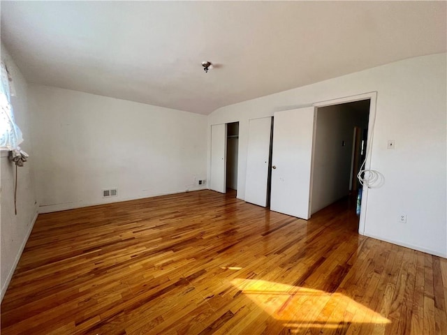 unfurnished bedroom featuring light wood-style floors, visible vents, and two closets