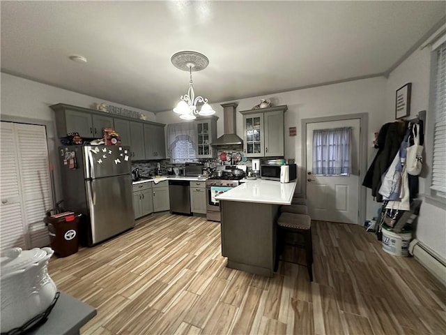 kitchen featuring glass insert cabinets, gray cabinets, stainless steel appliances, light countertops, and wall chimney range hood