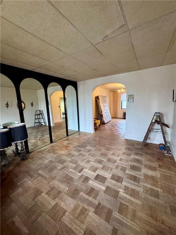 unfurnished room with a paneled ceiling, arched walkways, and baseboards