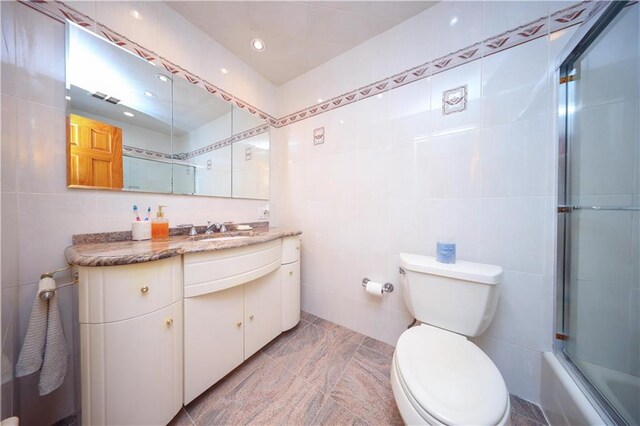 full bathroom featuring combined bath / shower with glass door, vanity, toilet, and tile walls