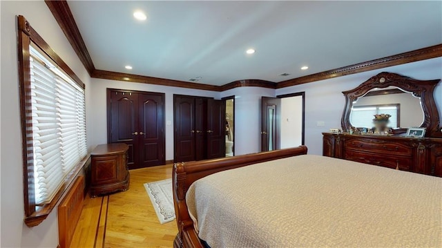 bedroom featuring light wood-type flooring, two closets, and ornamental molding