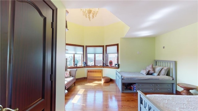 bedroom featuring light wood-type flooring, radiator, and a notable chandelier