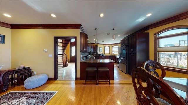 kitchen with a kitchen breakfast bar, stainless steel refrigerator, plenty of natural light, and ornamental molding