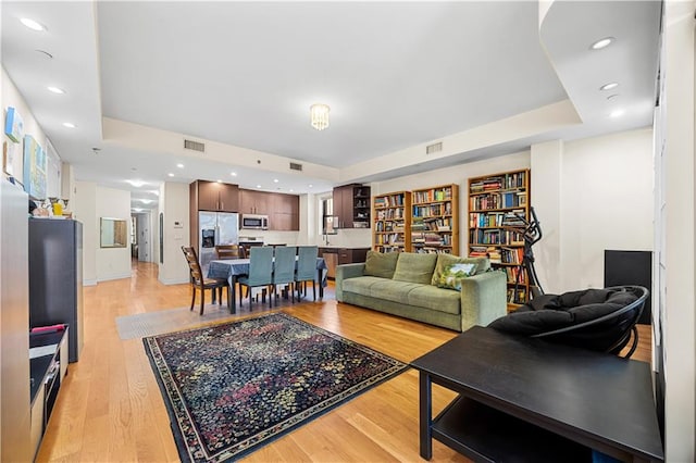 living room featuring a tray ceiling, light wood-type flooring, visible vents, and recessed lighting