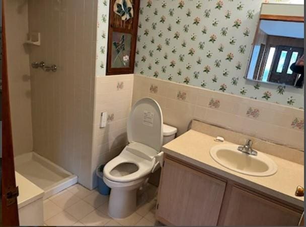 bathroom featuring walk in shower, tile patterned flooring, toilet, vanity, and tile walls