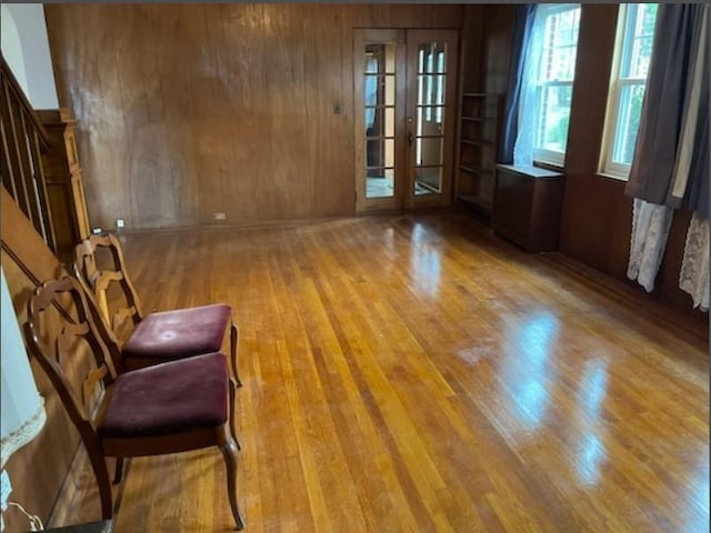 empty room featuring french doors, light hardwood / wood-style flooring, and wooden walls