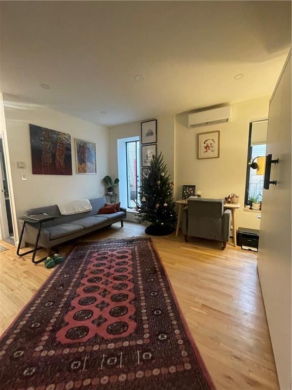 living room with a wall unit AC and light hardwood / wood-style flooring