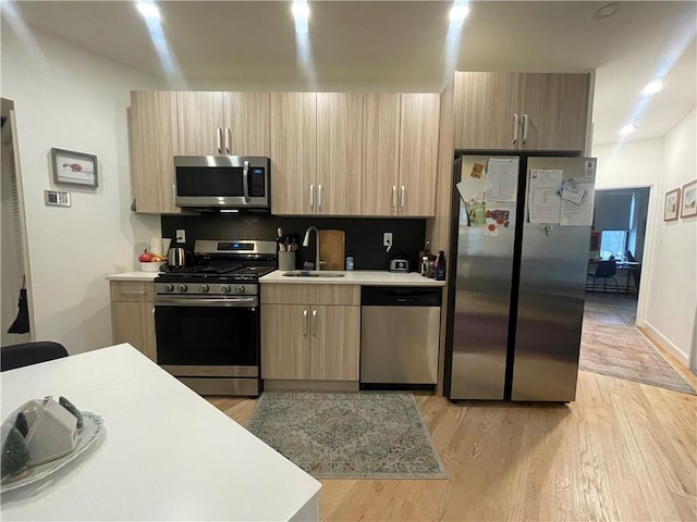 kitchen featuring sink, backsplash, stainless steel appliances, light wood-type flooring, and light brown cabinets