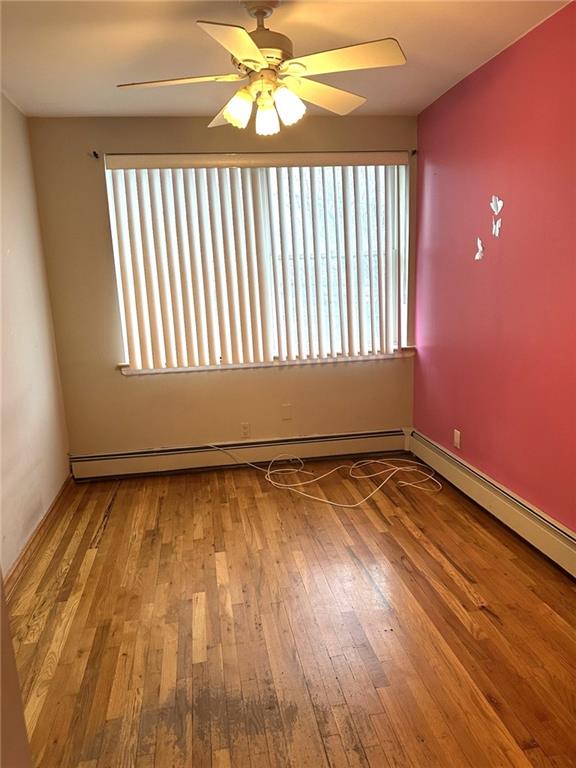 spare room featuring light hardwood / wood-style flooring, a baseboard radiator, and ceiling fan