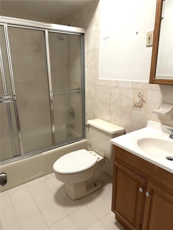 full bathroom with bath / shower combo with glass door, tile walls, tile patterned flooring, vanity, and toilet