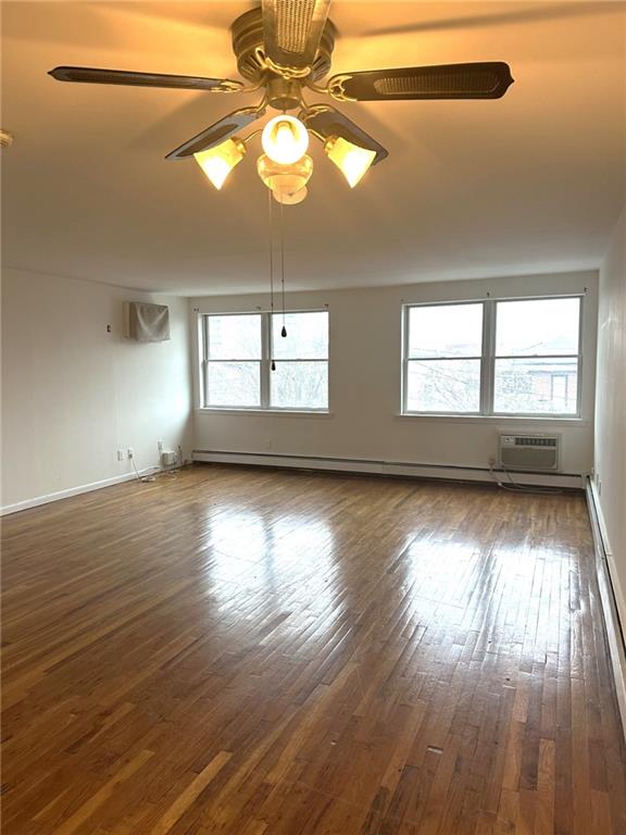 spare room featuring ceiling fan, dark wood-type flooring, an AC wall unit, and a healthy amount of sunlight