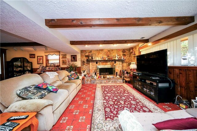 living room with beamed ceiling, a textured ceiling, a stone fireplace, and wooden walls