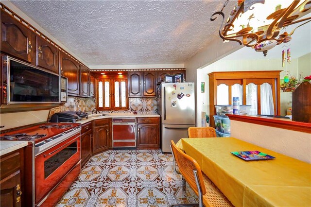 kitchen with decorative backsplash, appliances with stainless steel finishes, a textured ceiling, sink, and an inviting chandelier