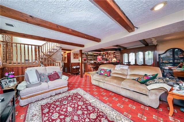 living room featuring carpet, wood walls, beamed ceiling, and a textured ceiling