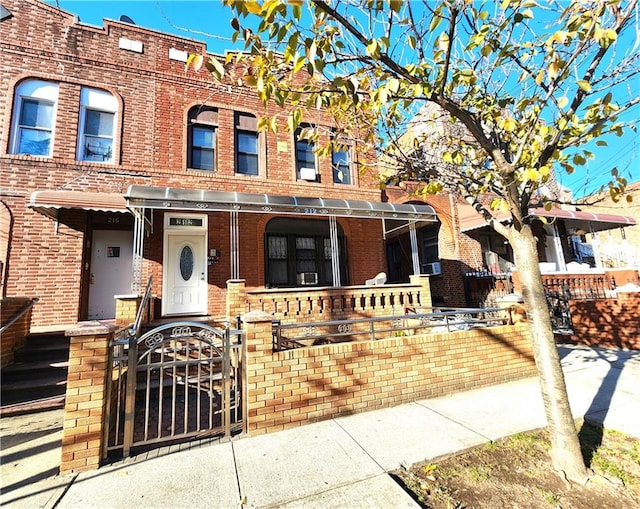 view of property featuring brick siding, a fenced front yard, a porch, and a gate