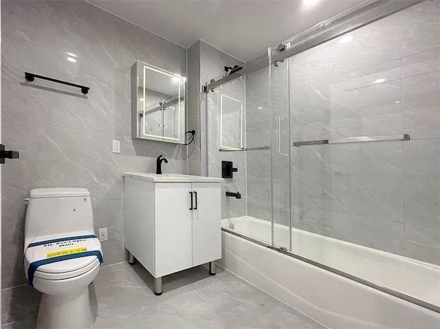 full bathroom with toilet, bath / shower combo with glass door, tile walls, vanity, and marble finish floor