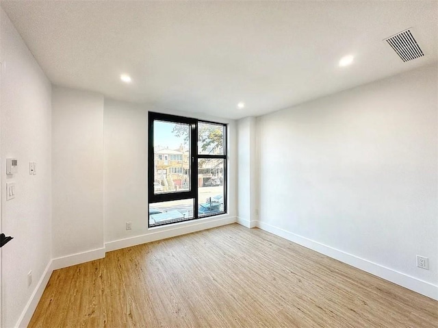 empty room featuring light wood-style floors, baseboards, visible vents, and recessed lighting