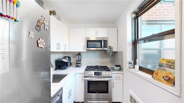 kitchen featuring stainless steel appliances, light stone counters, white cabinetry, and decorative backsplash