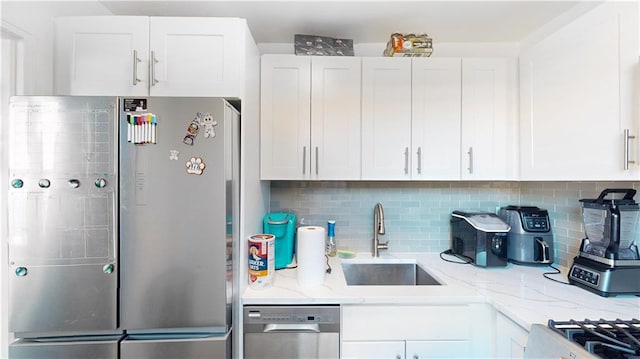 kitchen with light stone counters, stainless steel appliances, a sink, white cabinetry, and tasteful backsplash