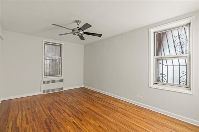 empty room with baseboards, ceiling fan, radiator heating unit, and wood finished floors