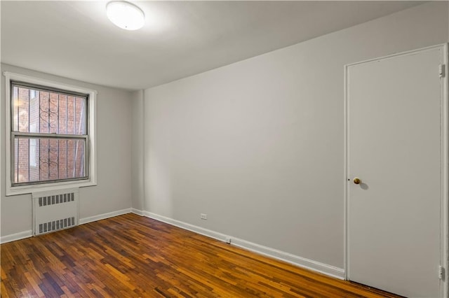 spare room with dark wood-type flooring, radiator, and baseboards
