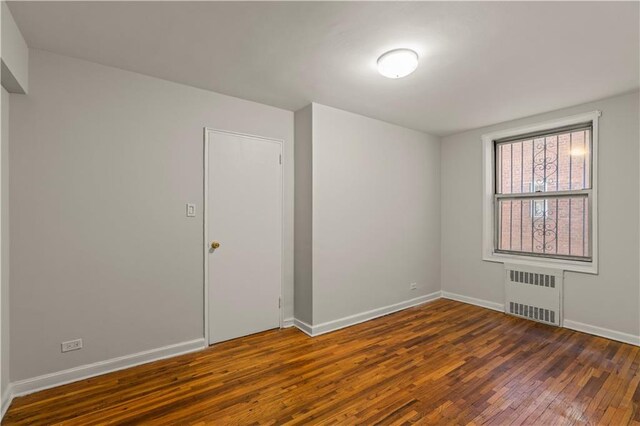 empty room with radiator heating unit, baseboards, and hardwood / wood-style flooring