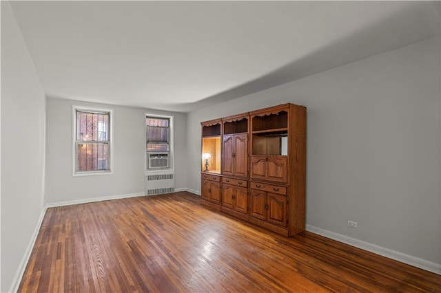 empty room featuring wood finished floors, baseboards, radiator heating unit, and cooling unit