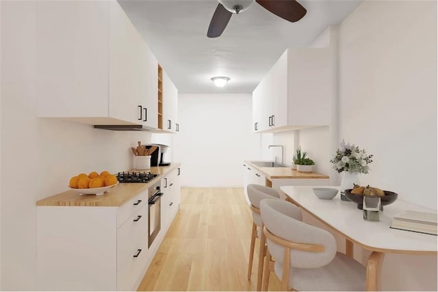 kitchen featuring gas cooktop, light wood-type flooring, a sink, white cabinetry, and oven