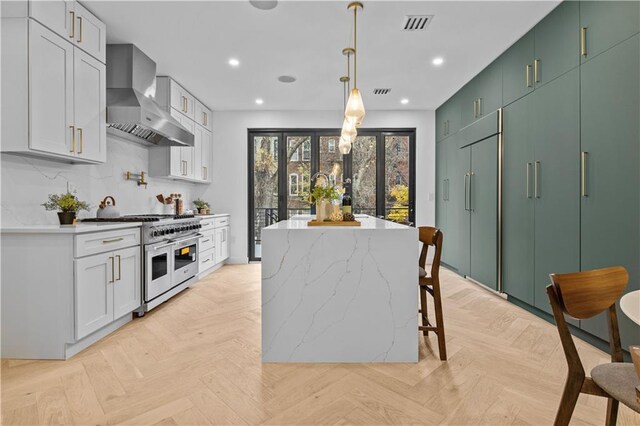 kitchen featuring double oven range, french doors, wall chimney range hood, white cabinetry, and light parquet flooring