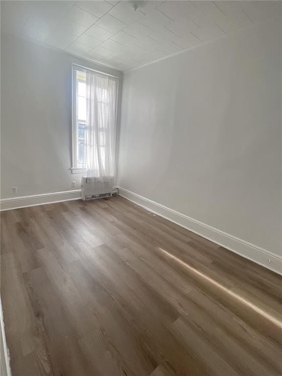 empty room with baseboards, dark wood-style flooring, and radiator heating unit