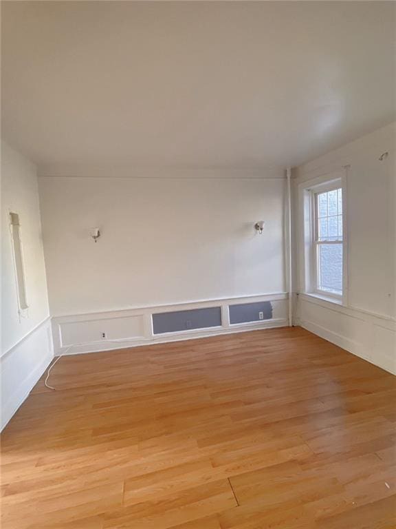 unfurnished room featuring light wood-type flooring, wainscoting, and a decorative wall