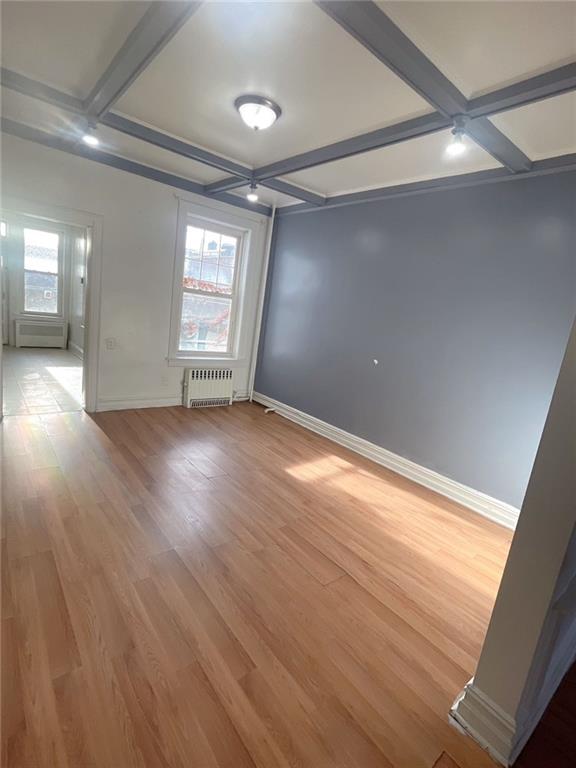 empty room with beamed ceiling, coffered ceiling, radiator heating unit, and plenty of natural light