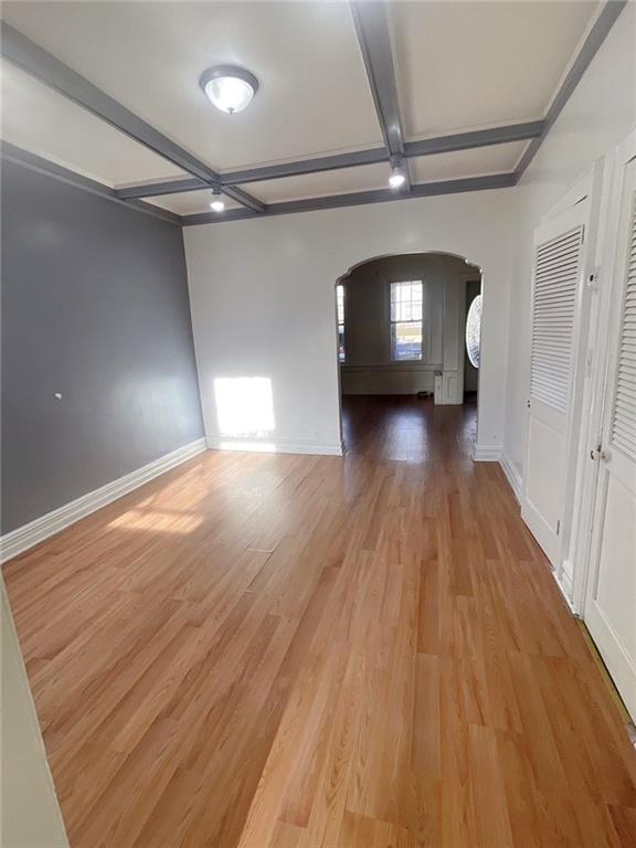 unfurnished room with baseboards, coffered ceiling, light wood finished floors, arched walkways, and beamed ceiling