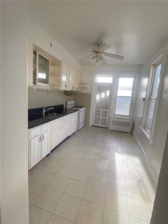 kitchen featuring dark countertops, open shelves, ceiling fan, white gas range, and a sink