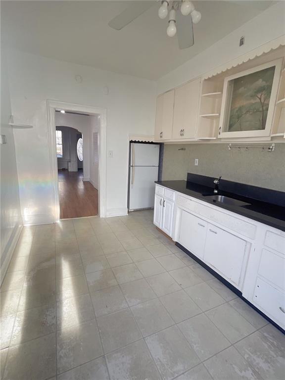 kitchen featuring open shelves, freestanding refrigerator, a sink, white cabinets, and dark countertops