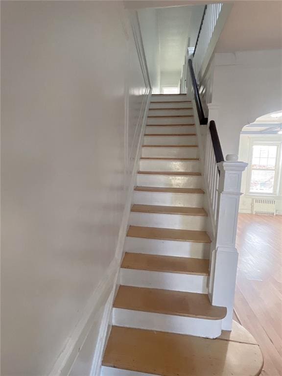 staircase featuring radiator, wood finished floors, and arched walkways