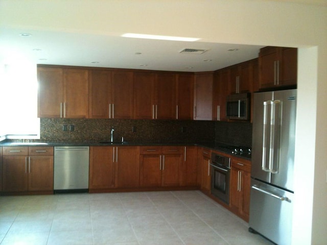 kitchen featuring visible vents, brown cabinetry, dark countertops, appliances with stainless steel finishes, and a sink